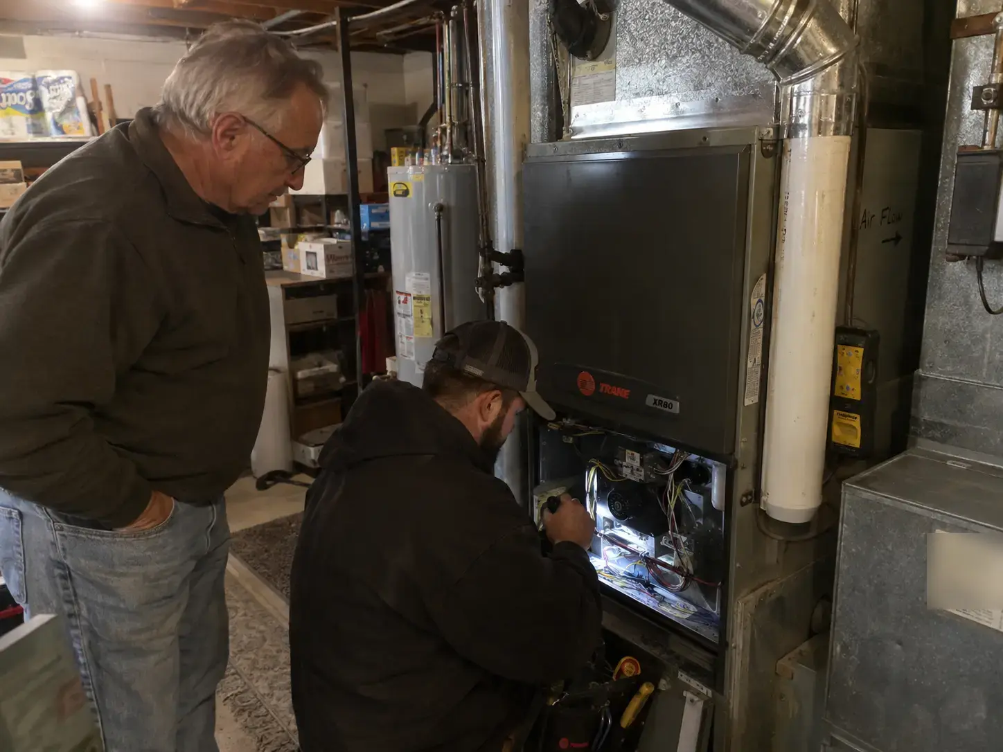 Technician inspecting the blower compartment of a basement furnace with a work light