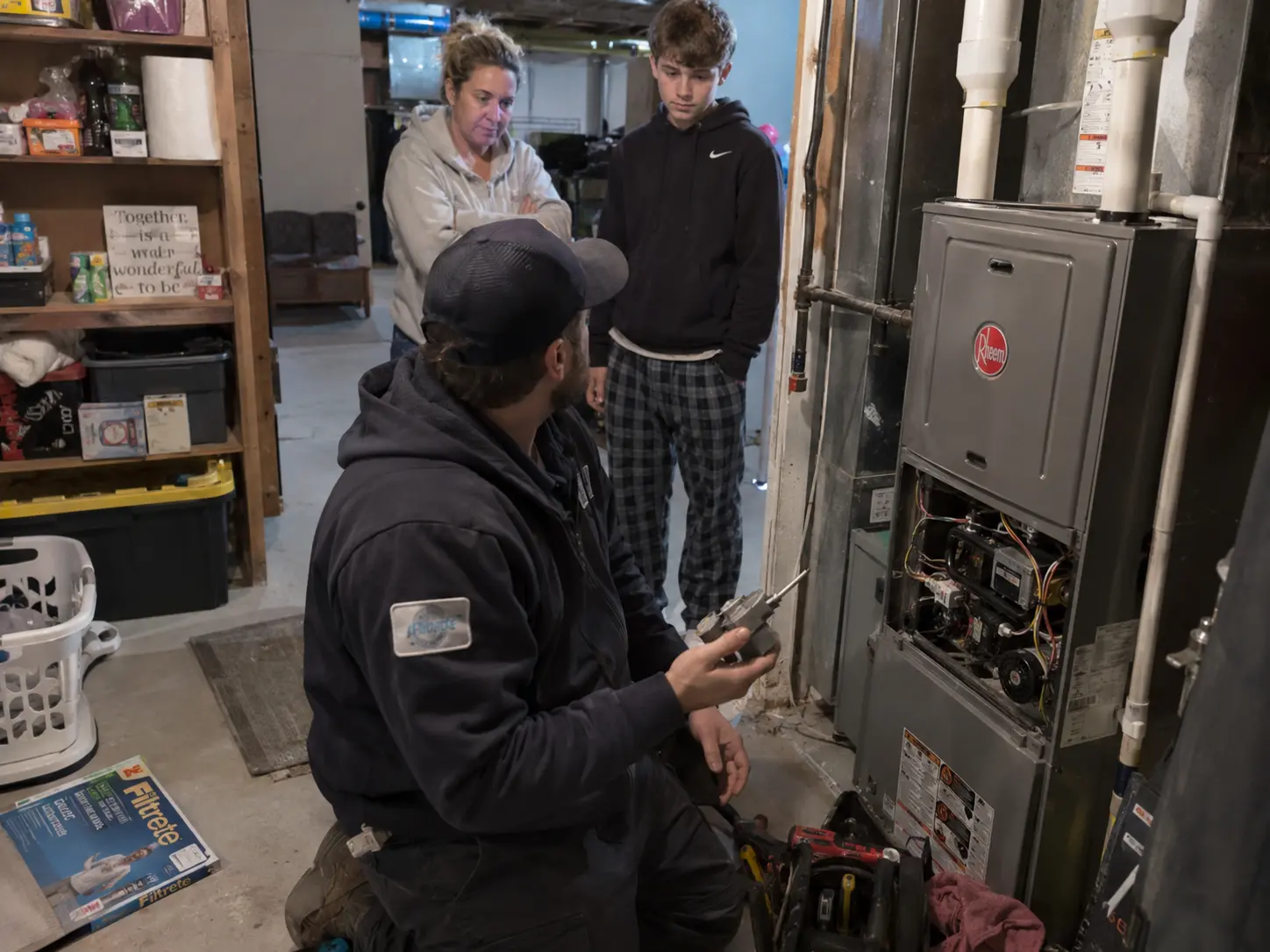 Technician holding a furnace component while explaining the finding to a family