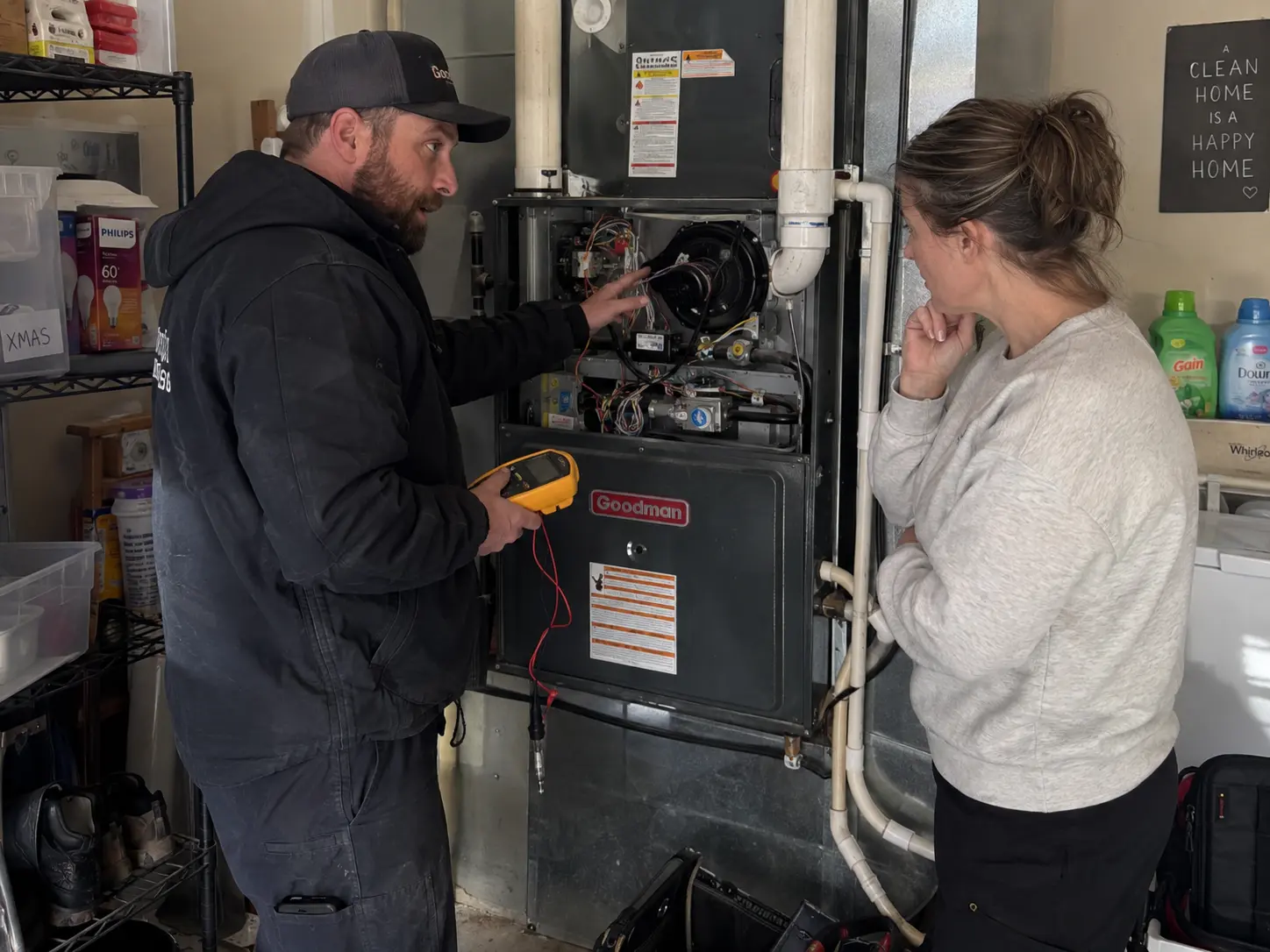 Technician pointing out the draft inducer assembly to a homeowner in a laundry room